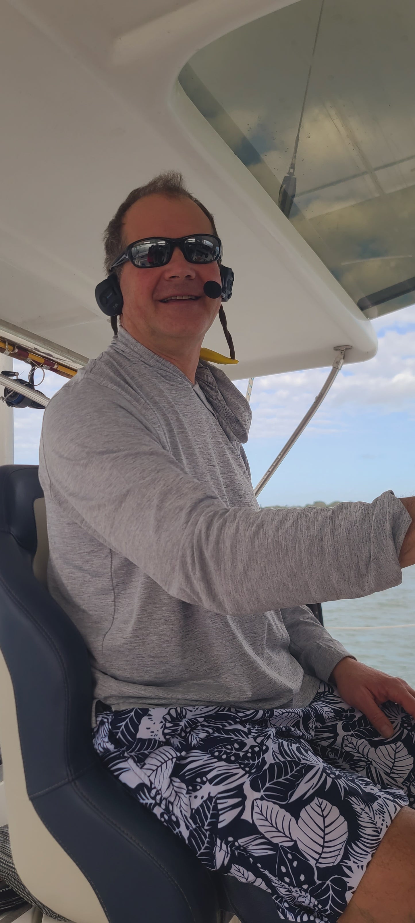 Image of the captain on a boat wearing the 2Talk bluetooth communication headset. He is talking to his crew at the front of the boat. He is able to wear sunglasses with the headsets.