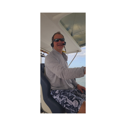 Image of the captain on a boat wearing the 2Talk bluetooth communication headset. He is talking to his crew at the front of the boat. He is able to wear sunglasses with the headsets.